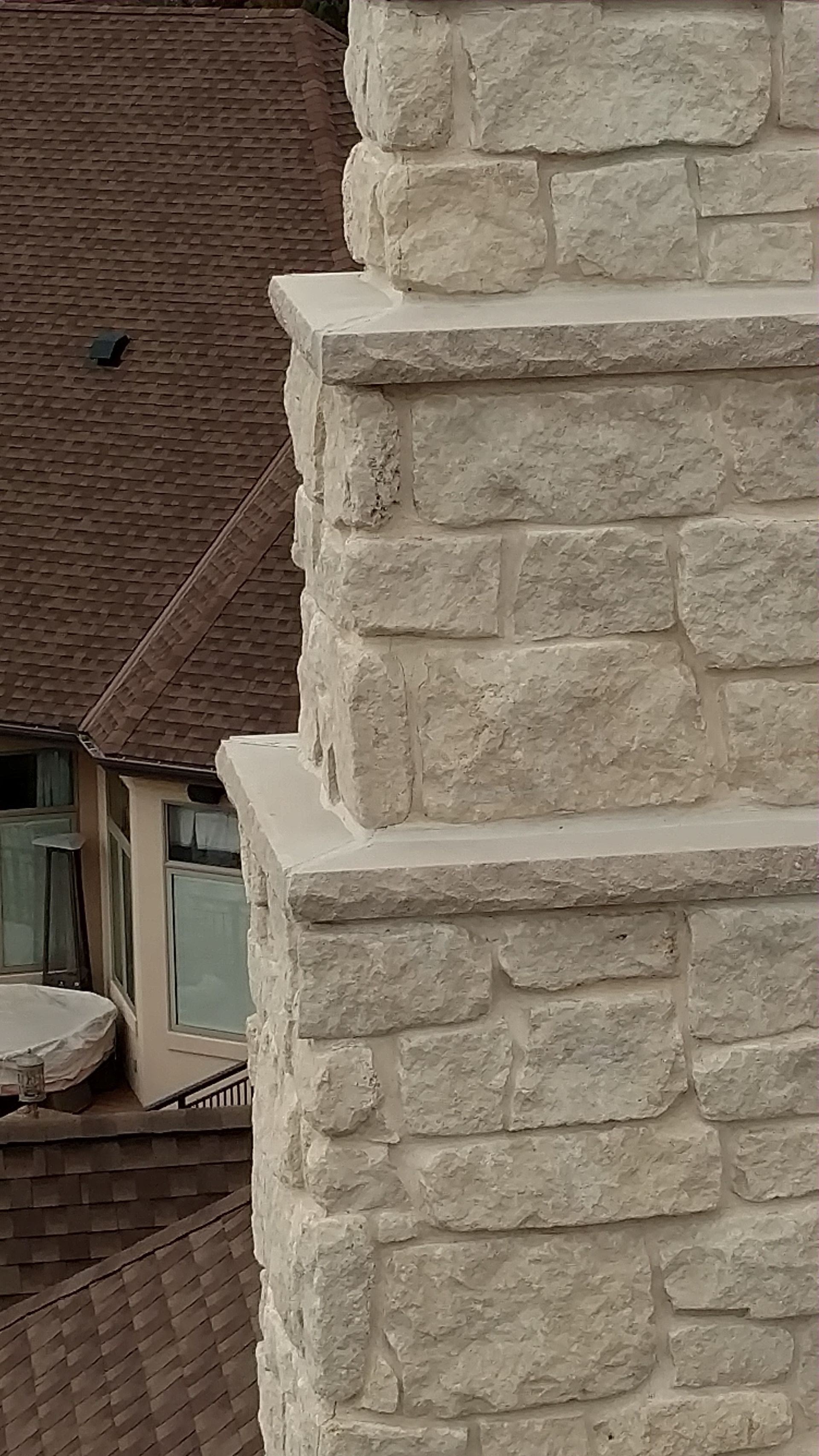 Stone chimney on the exterior of a building with a brown shingled wall in the background