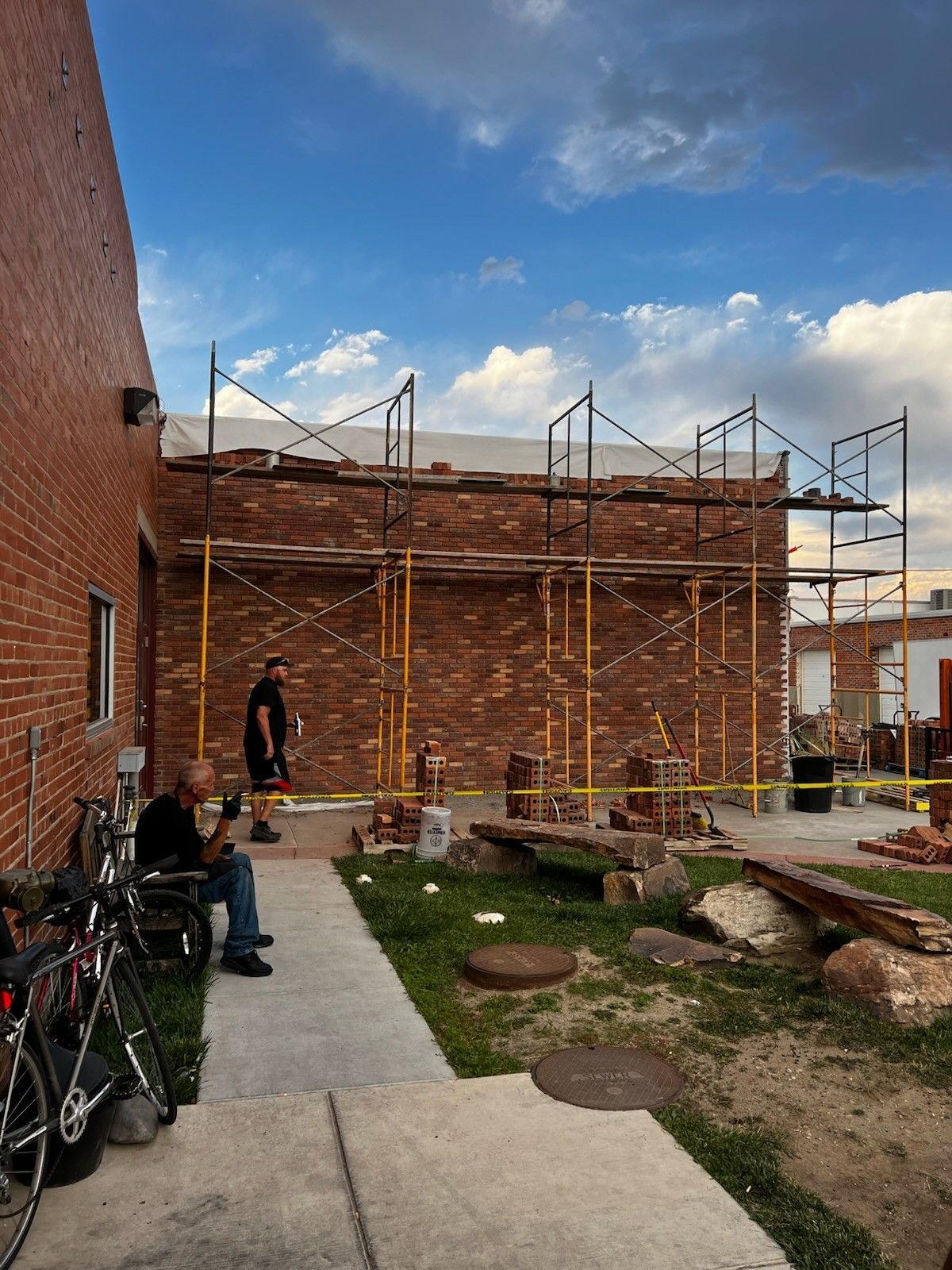 Outdoor courtyard with brick walls, scaffolding, benches, and a person walking along a paved path