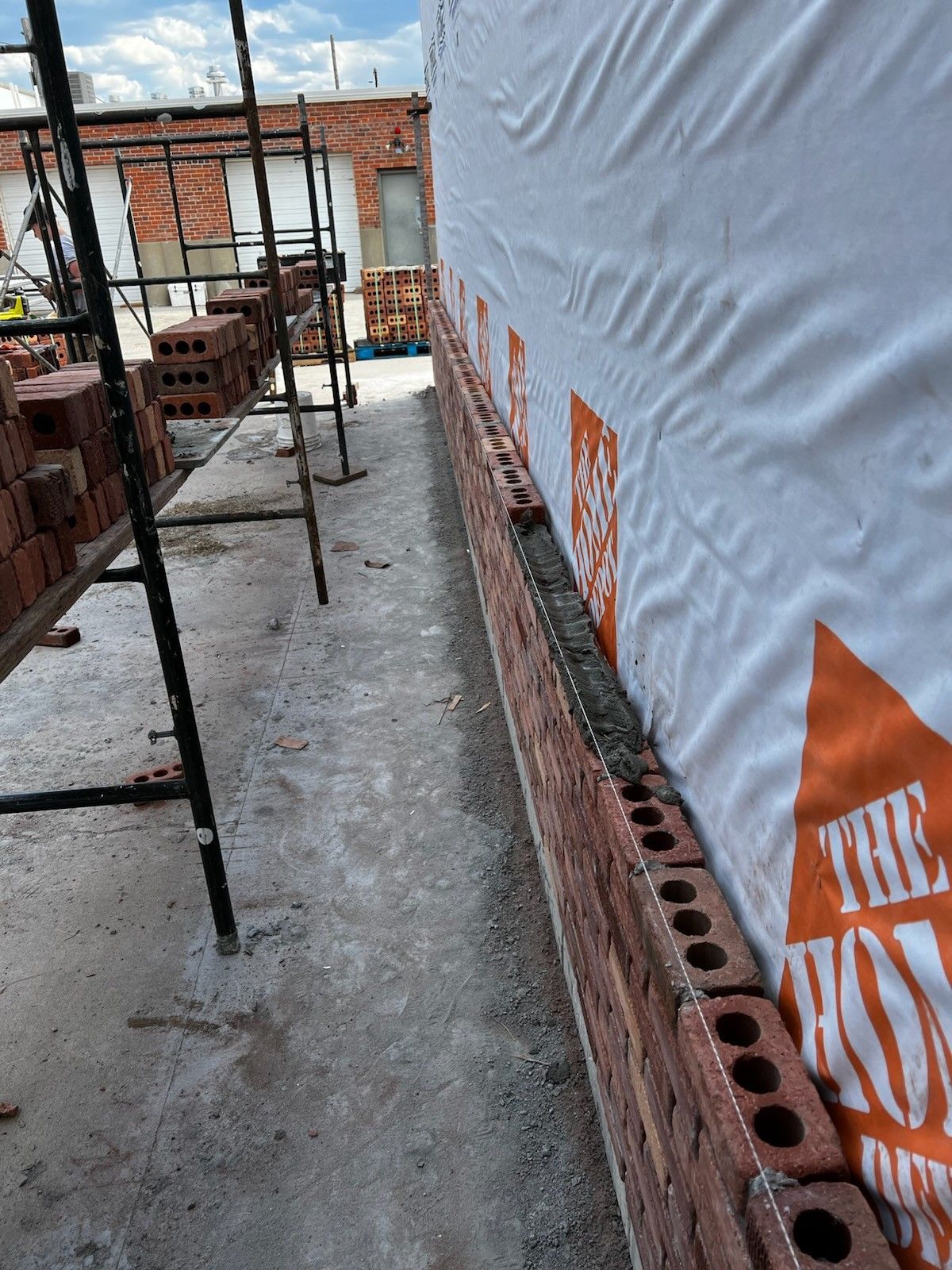 Construction walkway beside a white tarp wall, with stacked bricks and scaffolding on the left.