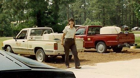 Woman standing near two pickup trucks parked on gravel driveway.