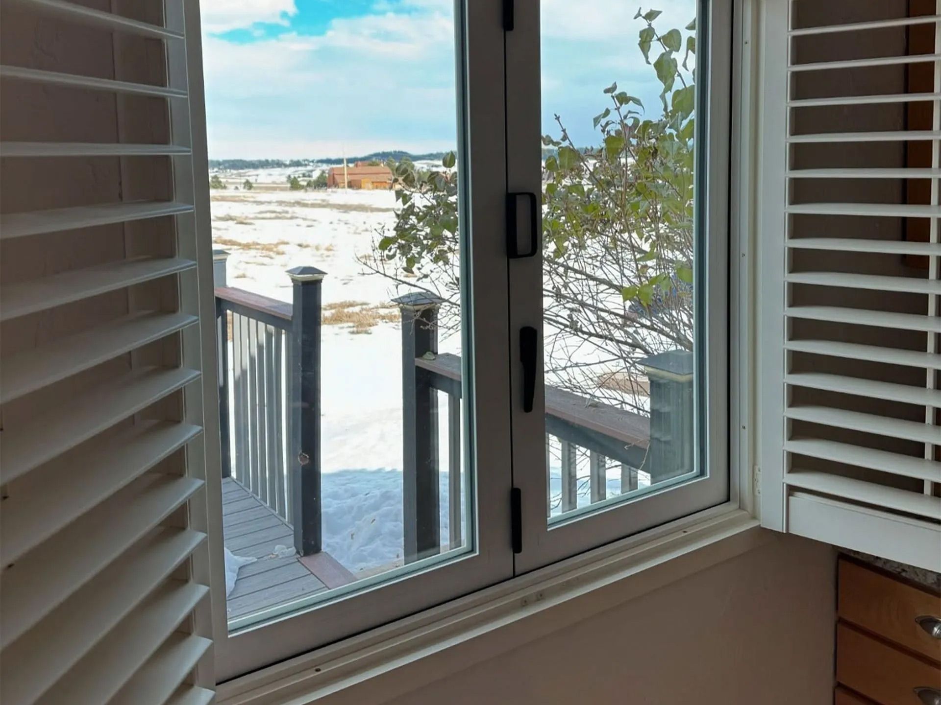 A window with shutters open and a view of a deck