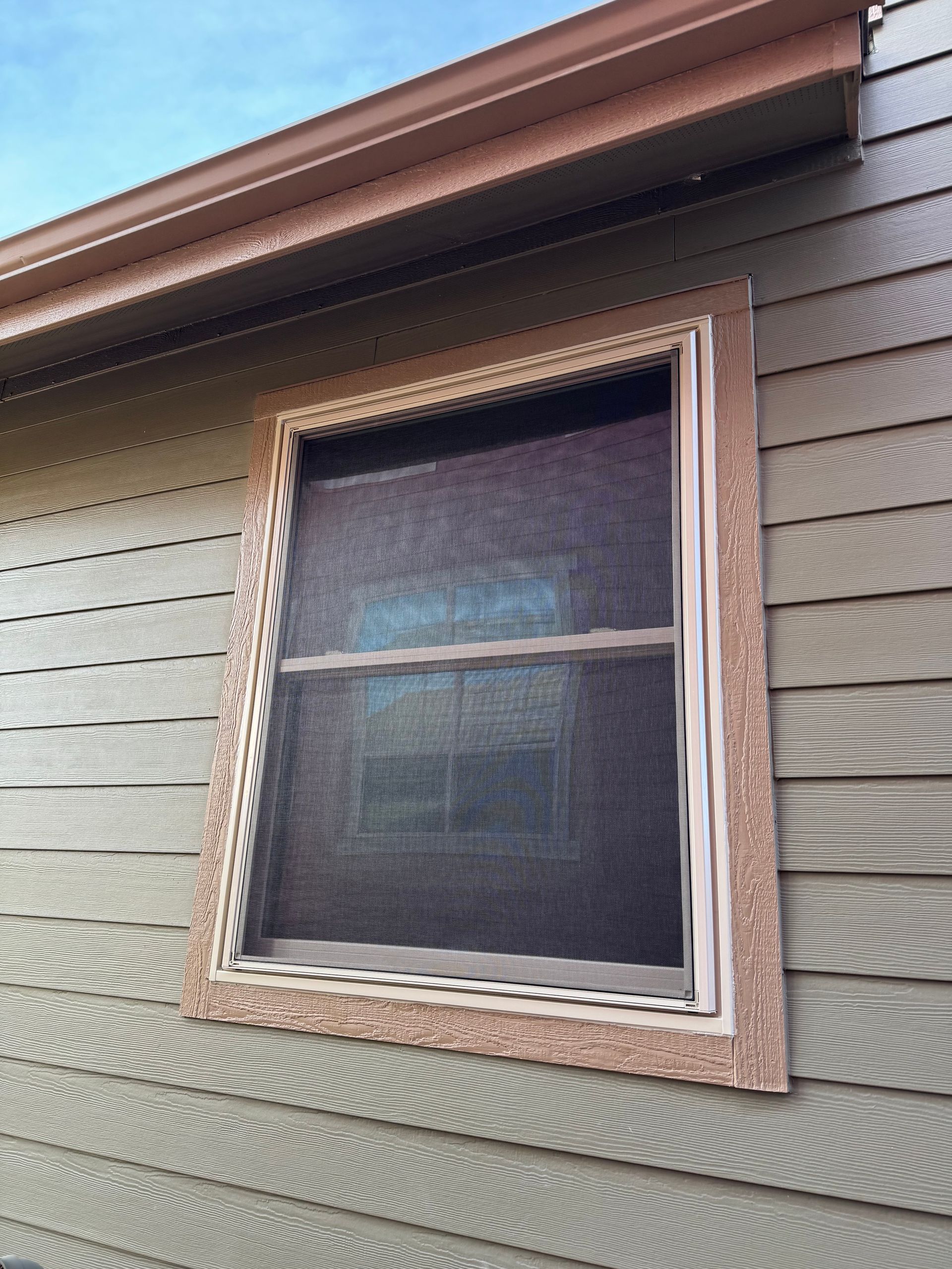 A window with a screen on it is on the side of a house.