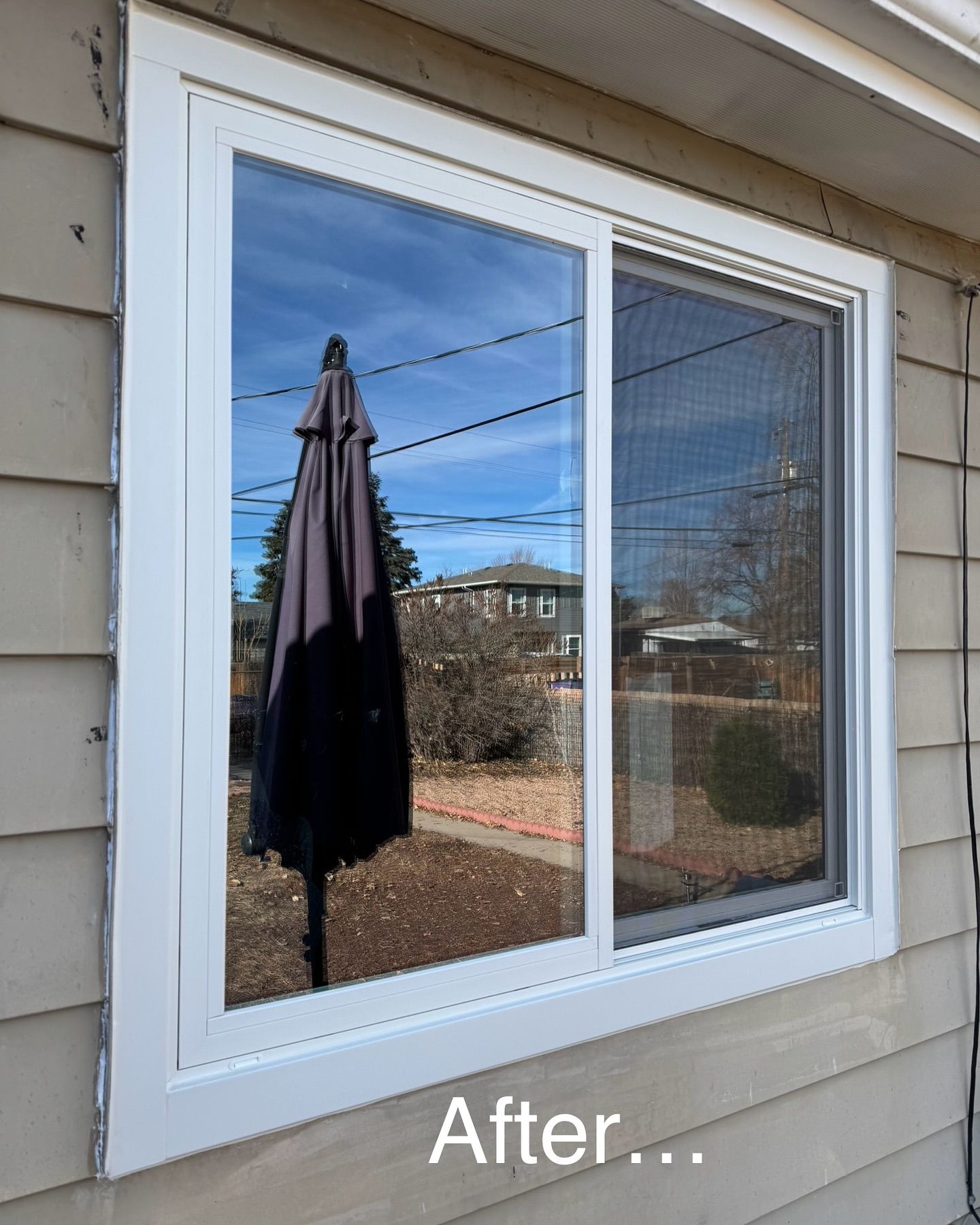 A white window on the side of a house with a black umbrella in the window.