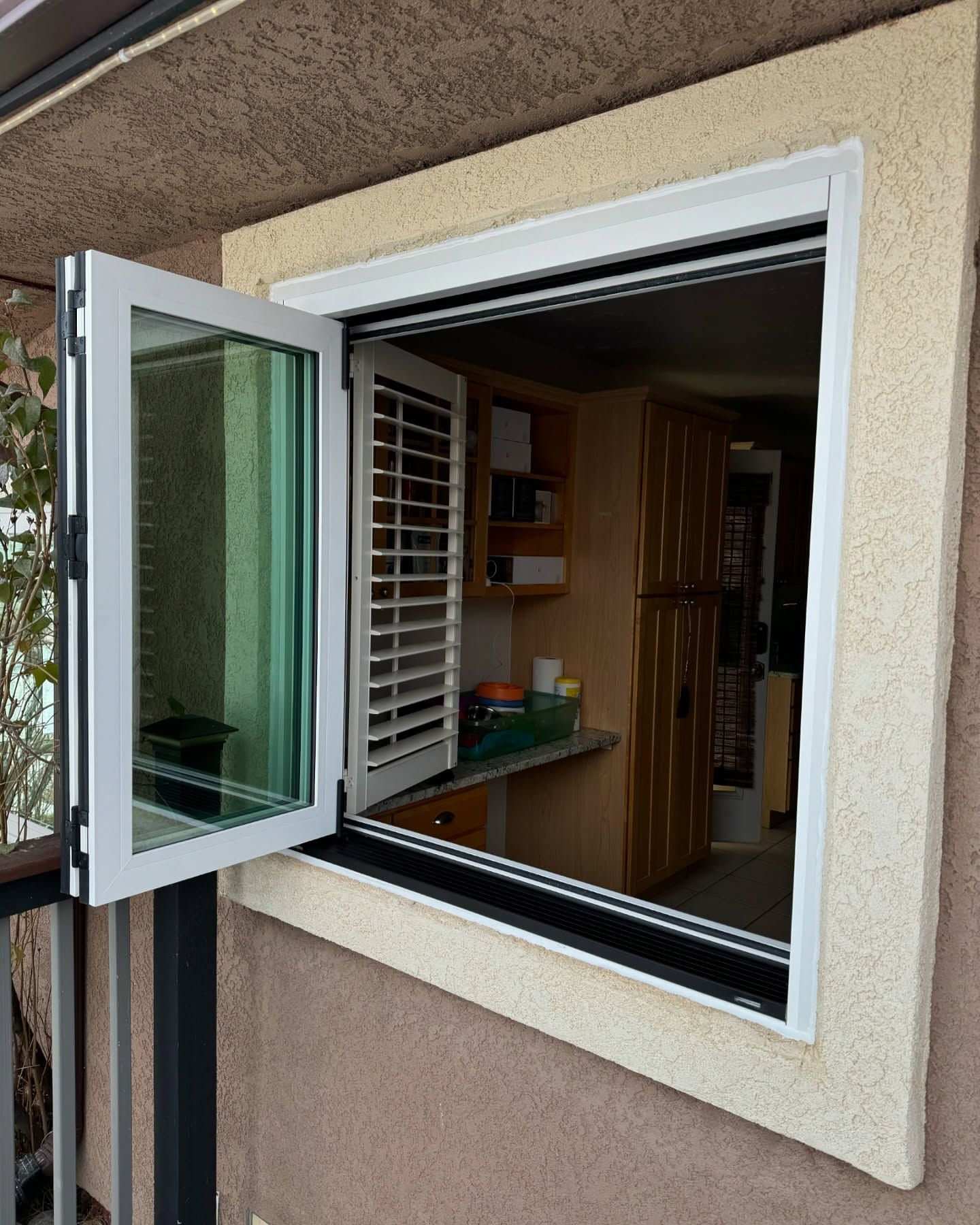 A window with shutters on it is open to a kitchen.