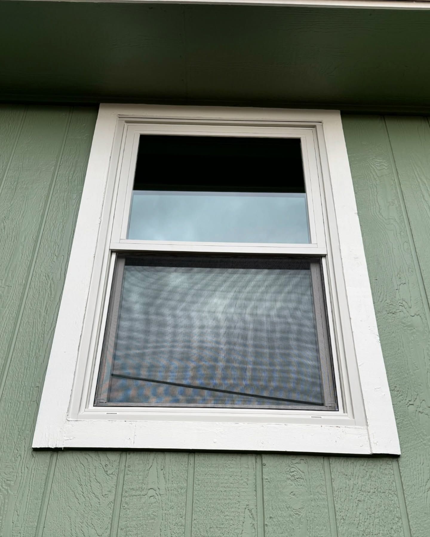 A window with a screen on it is on a green building.
