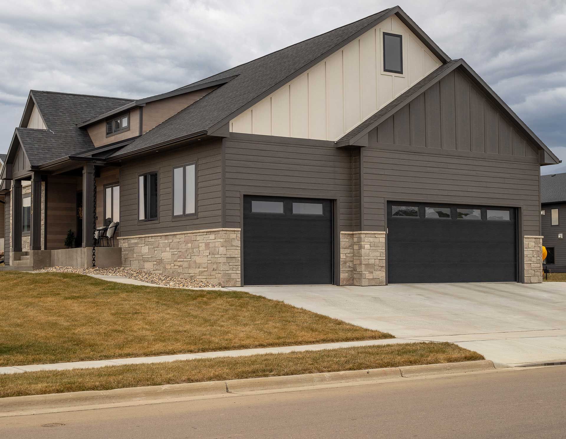 a large house with two black garage doors and a concrete driveway