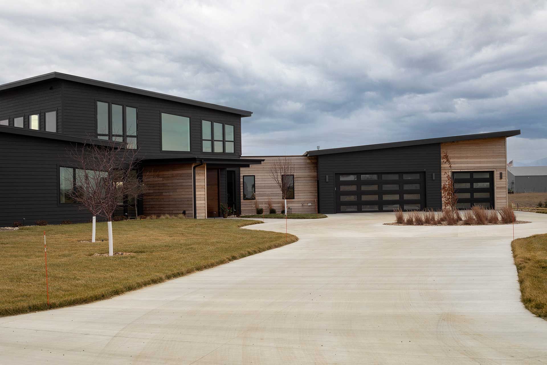a large black house with wooden elements and a concrete driveway in front of it