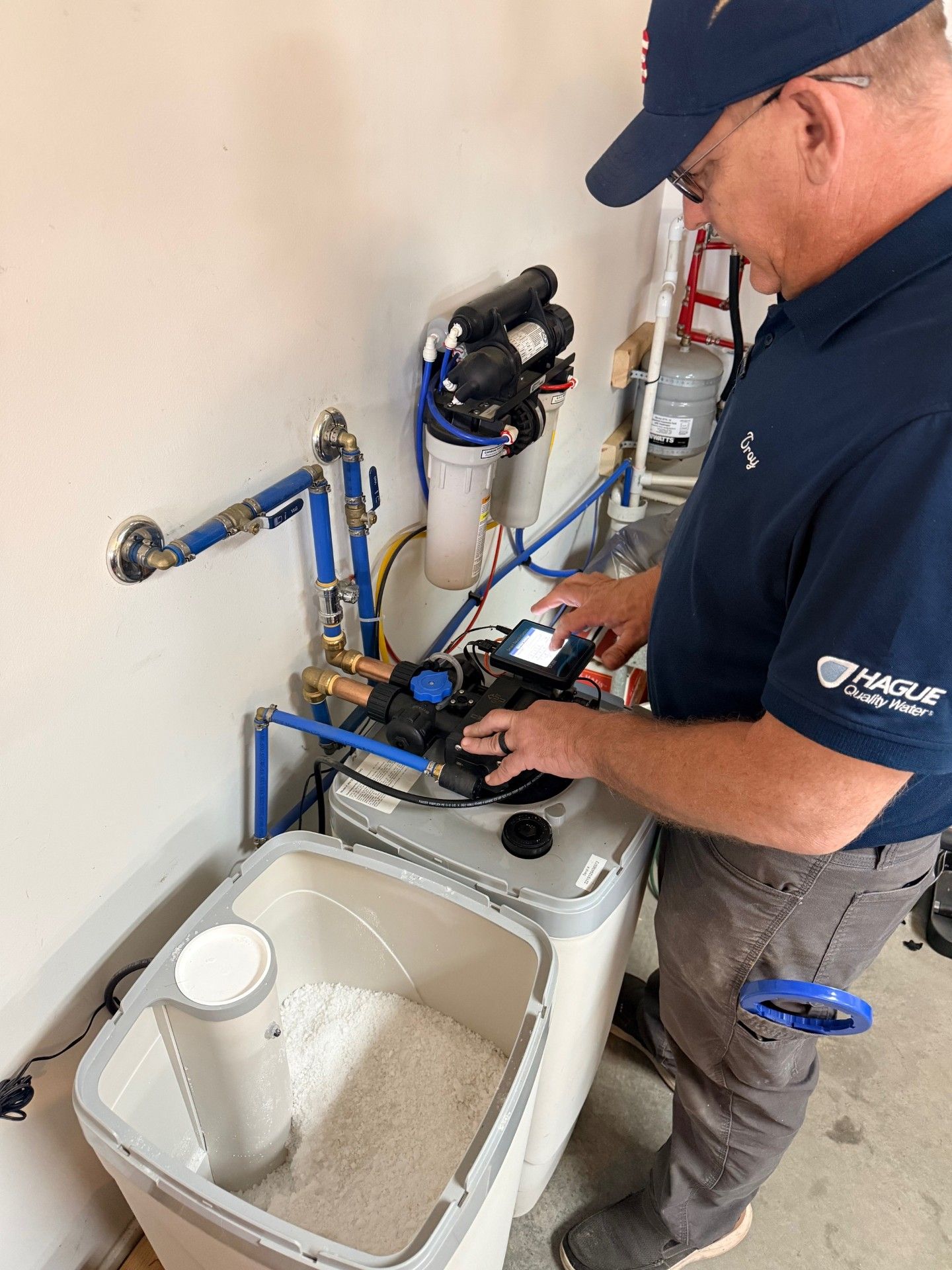 A person in a blue shirt adjusting the digital display on a home water softening system.