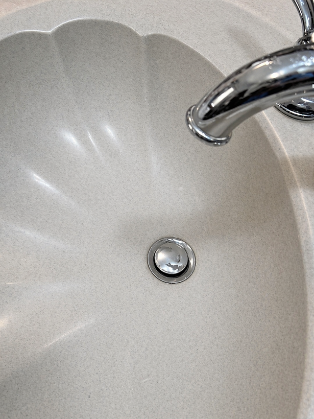 Close-up of a white bathroom sink with a chrome faucet and drain stopper.