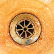 Metal sink drain surrounded by heavy orange rust and mineral buildup