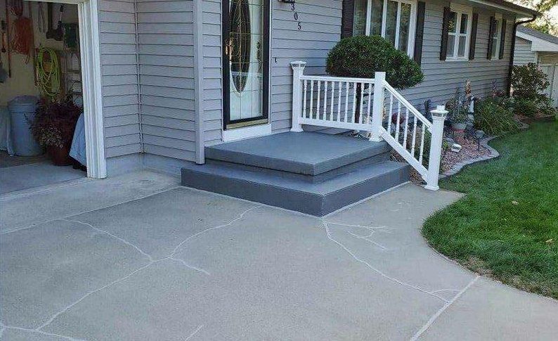 A concrete porch with stairs and a white railing in front of a house