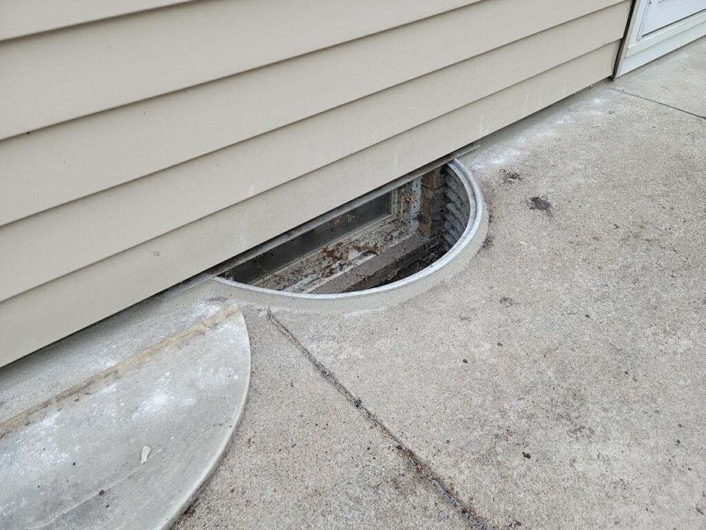 A window well in the side of a house on a sidewalk