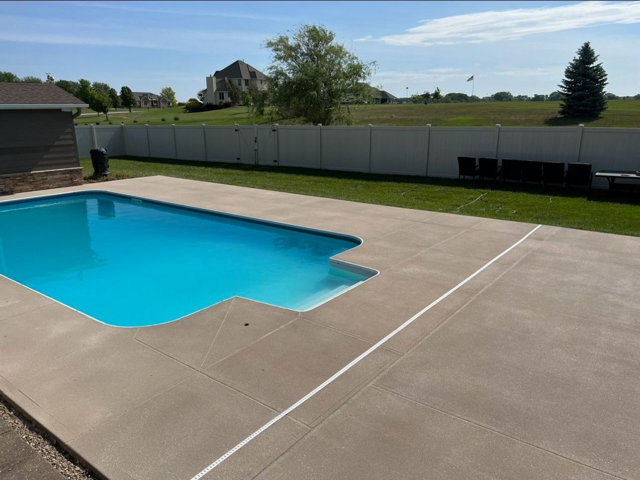 A large swimming pool in a backyard with a white fence