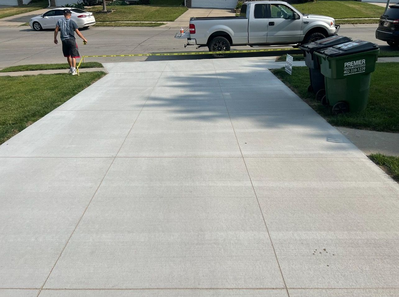 A man is walking down a concrete driveway next to a truck and a trash can