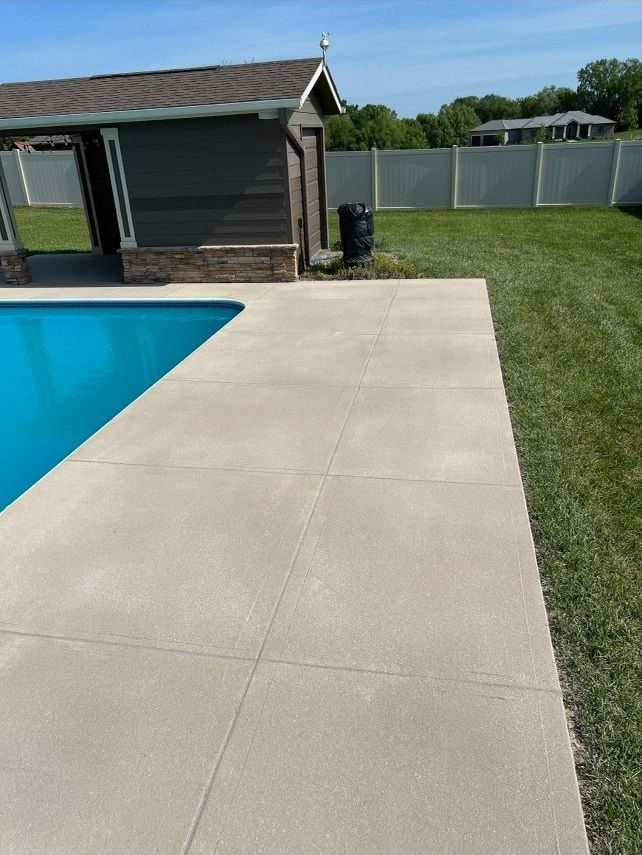 A concrete patio next to a swimming pool with a house in the background