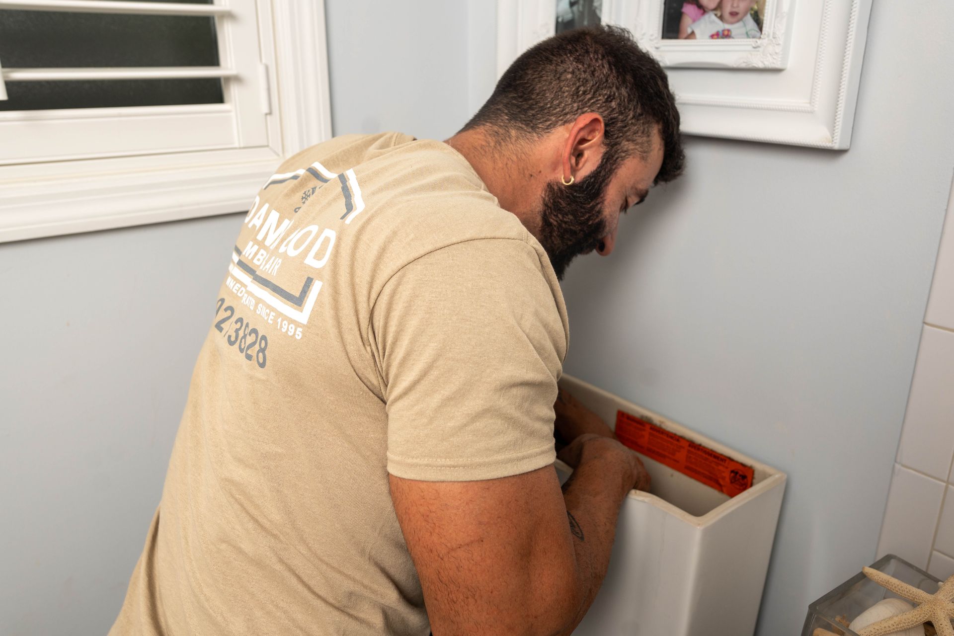 Man in tan shirt installing a white sink in a bathroom.