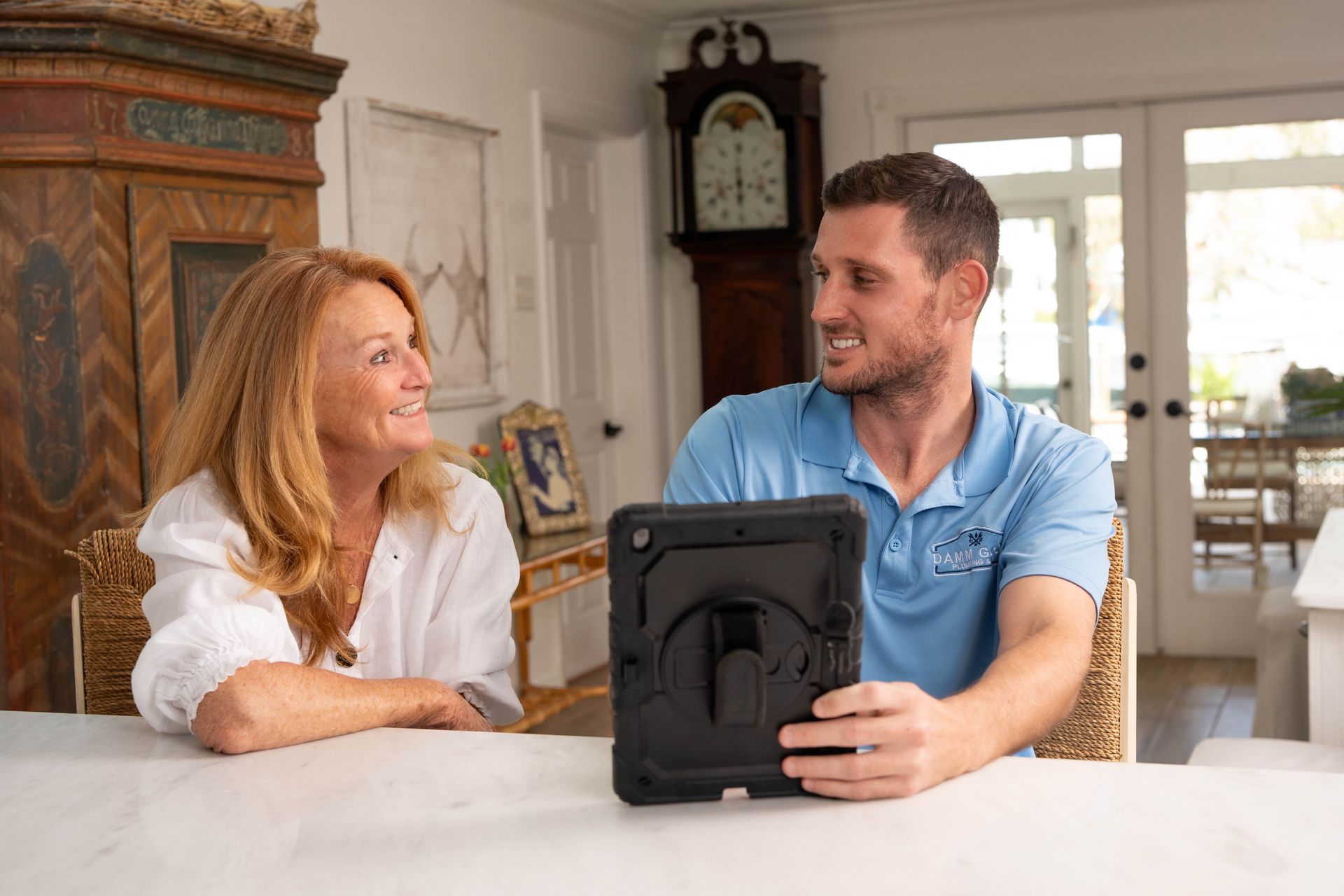 Woman and man looking at tablet. They sit at a table in a bright room. The man holds the tablet.