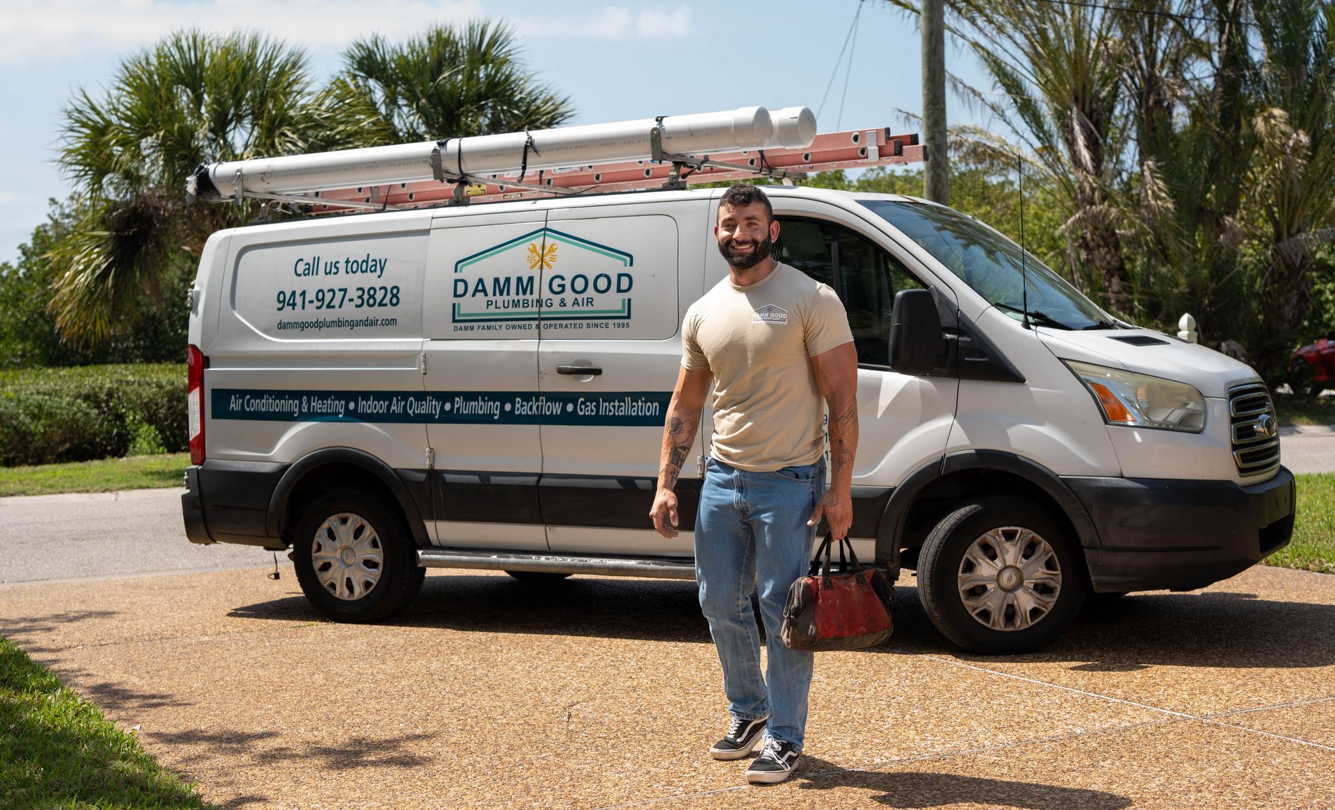 Man standing by a work van with ladder on top. The van has business logo with phone number.