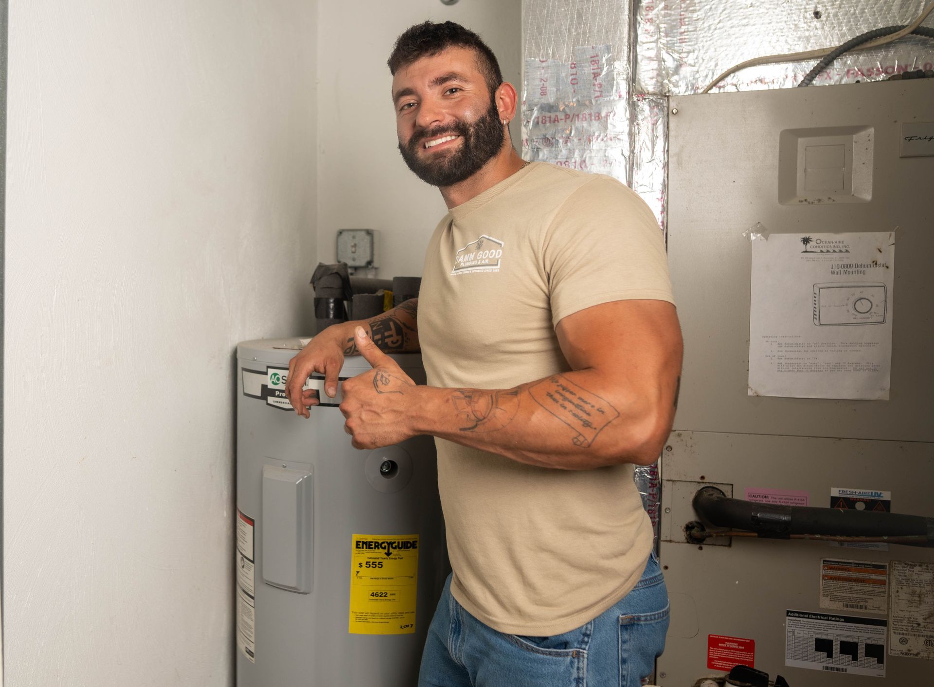 Man in tan shirt gives thumbs up next to a water heater and HVAC unit.