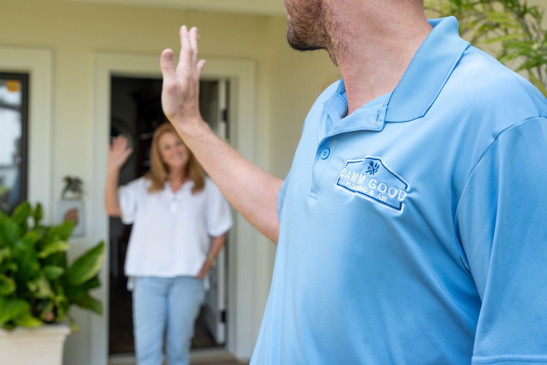 Man in blue shirt waves goodbye to a woman at a doorway.