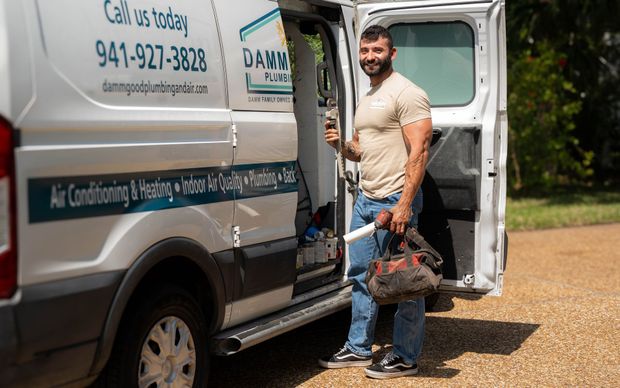 HVAC technician with tools beside a van.  Text on the van includes phone number, services, and company name.
