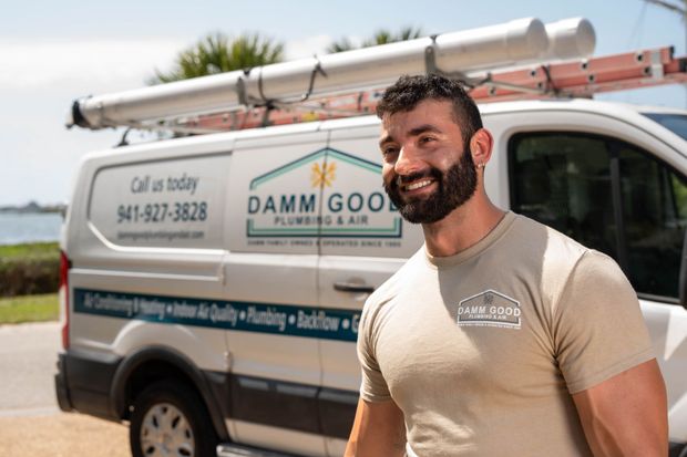 Smiling man standing next to a Damm Good Plumbing van. White van with ladder, logo, and phone number.