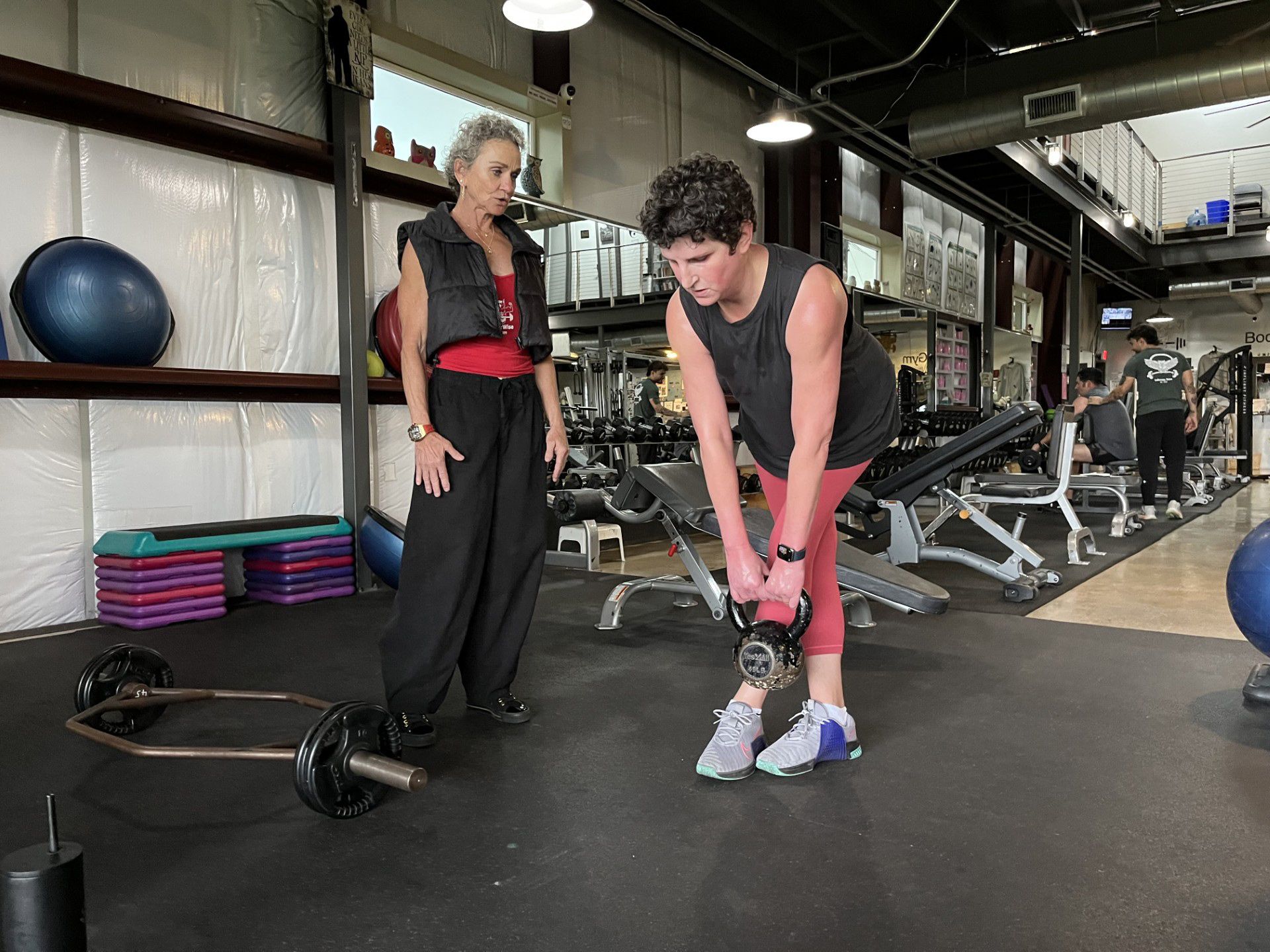 A woman is standing next to a man lifting a dumbbell in a gym.