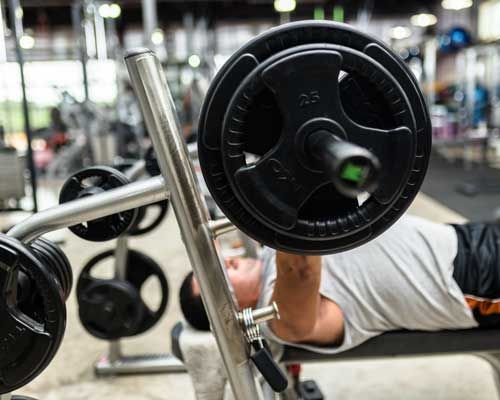 A man is lifting a barbell on a bench in a gym.