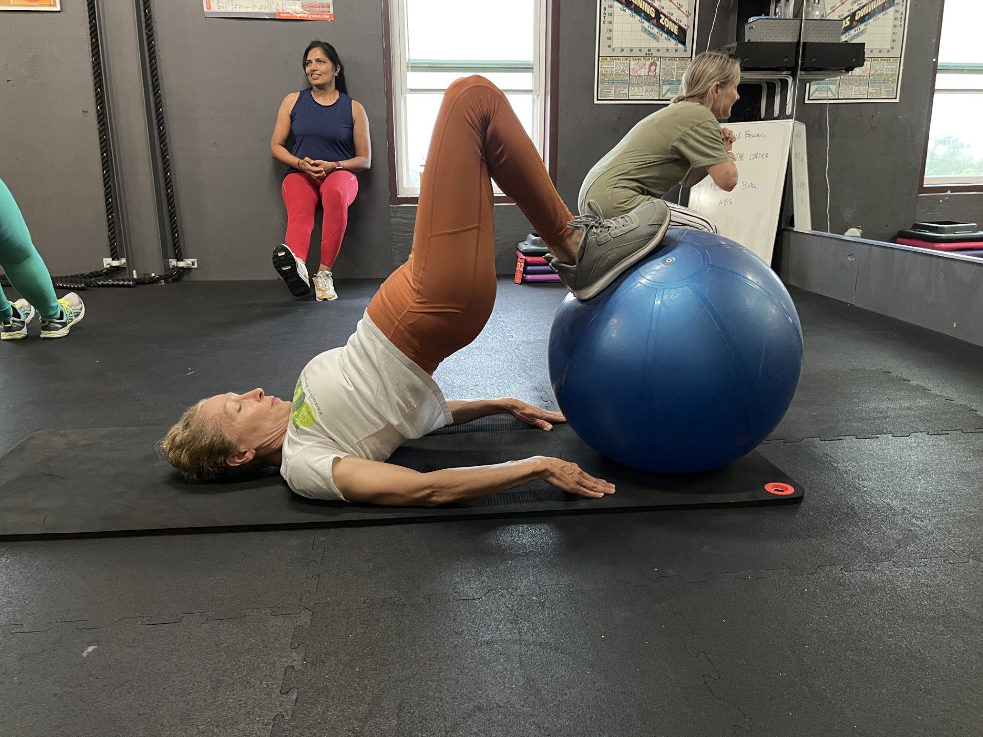 A woman is doing exercises on a blue exercise ball in a gym.