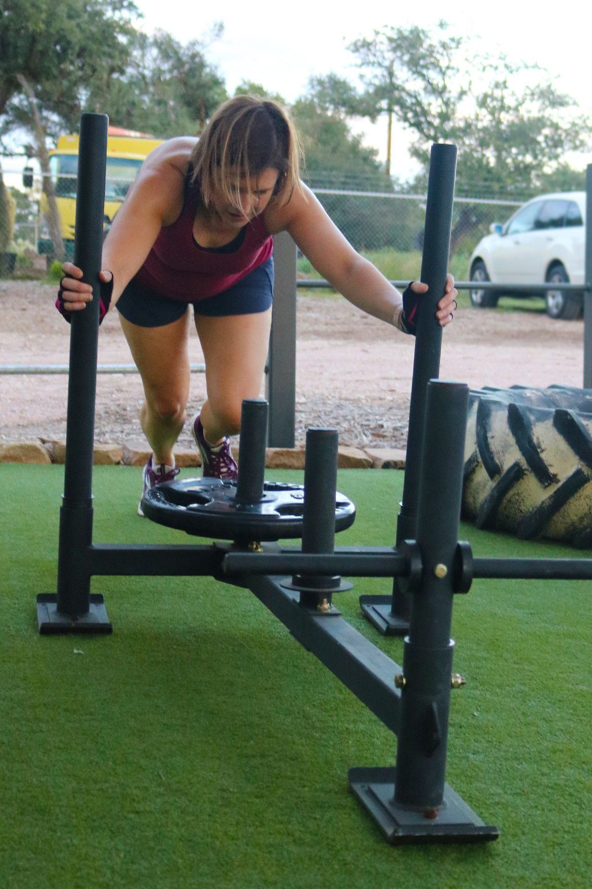 A woman is pushing a sled with a tire in the background.