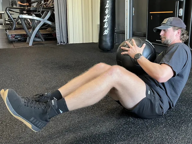 A man is doing a crunch with a medicine ball in a gym.