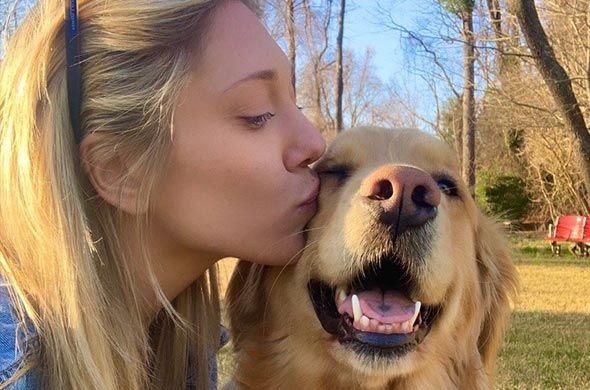 A woman is kissing a dog on the nose.