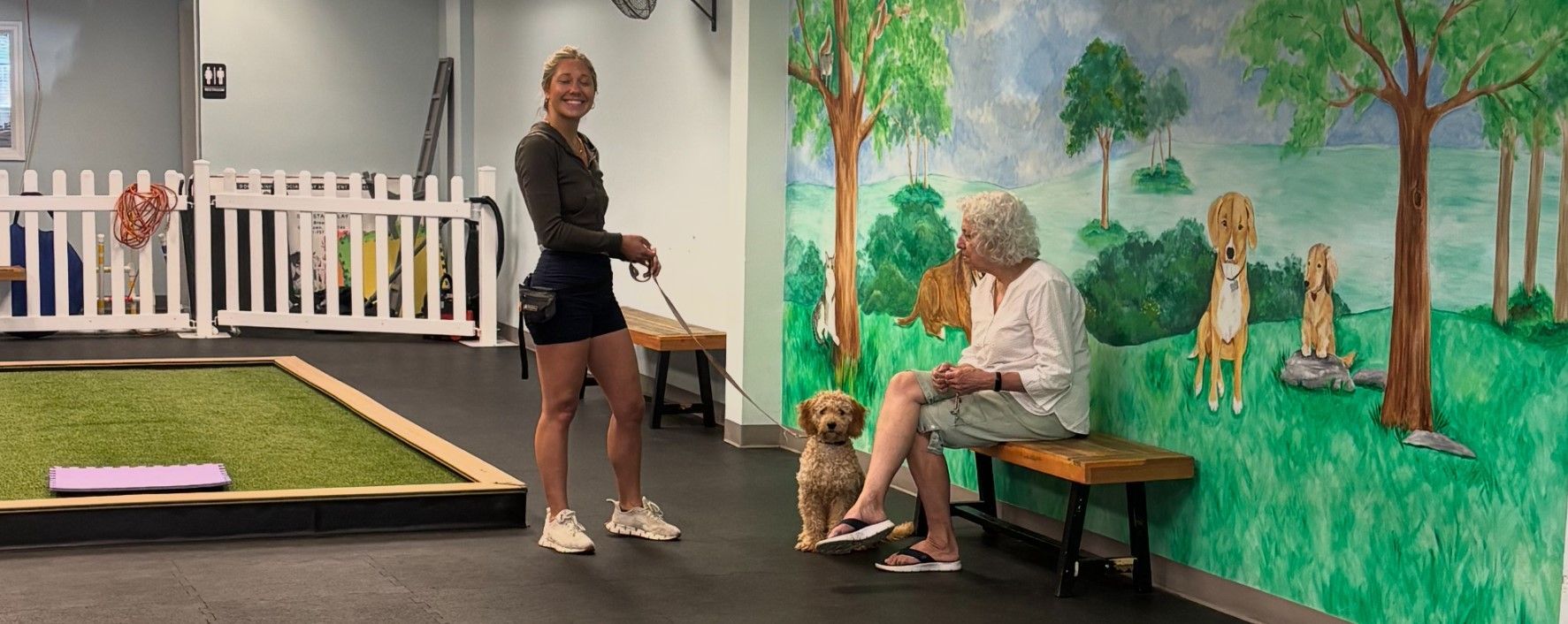 A woman is standing next to a woman sitting on a bench with a dog.