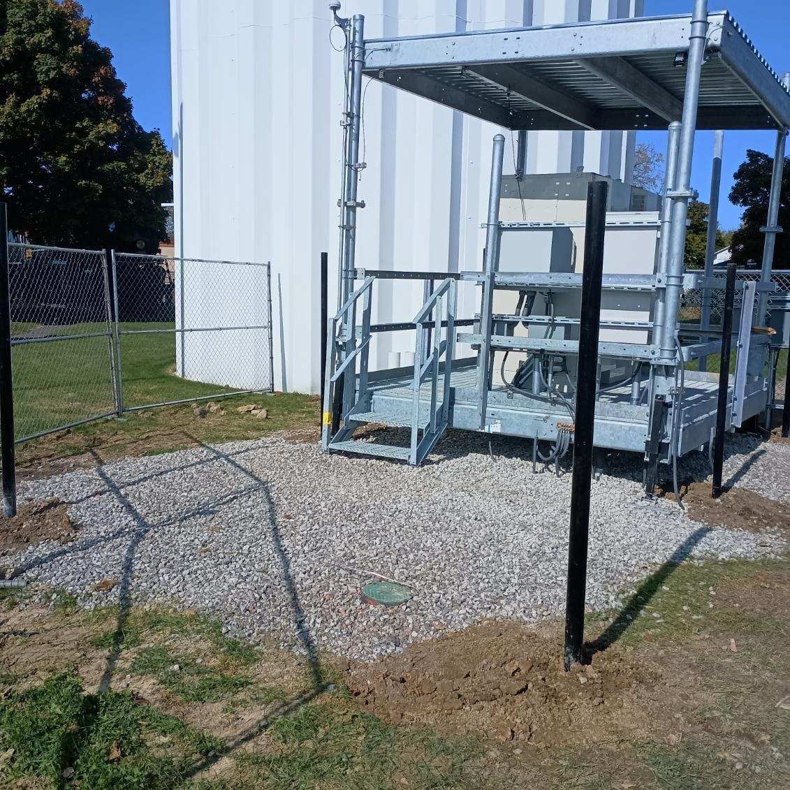 A metal structure with stairs is surrounded by gravel and a chain link fence
