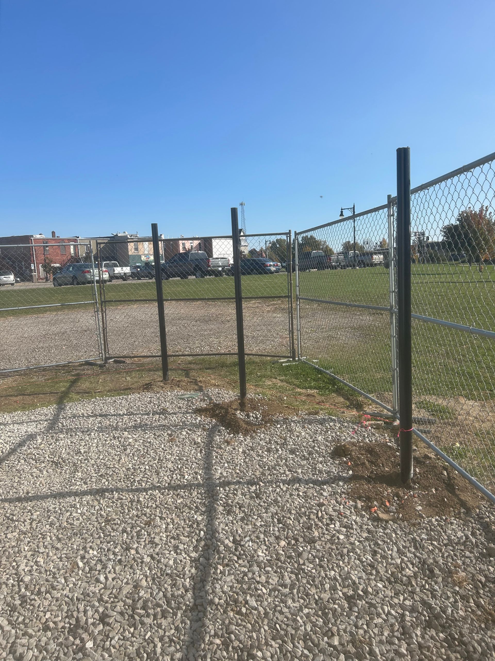A chain link fence surrounds a gravel area in a park