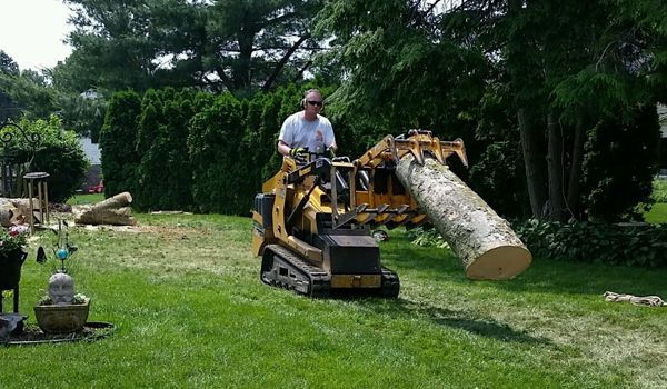 A man is driving a tractor with a large log in the backyard