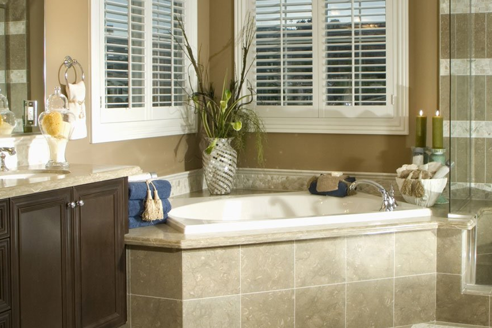 A bathroom with a tub , sink , mirror and shutters.