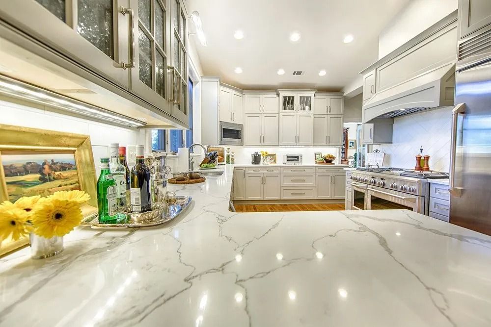 A kitchen with white cabinets , stainless steel appliances , and marble counter tops.