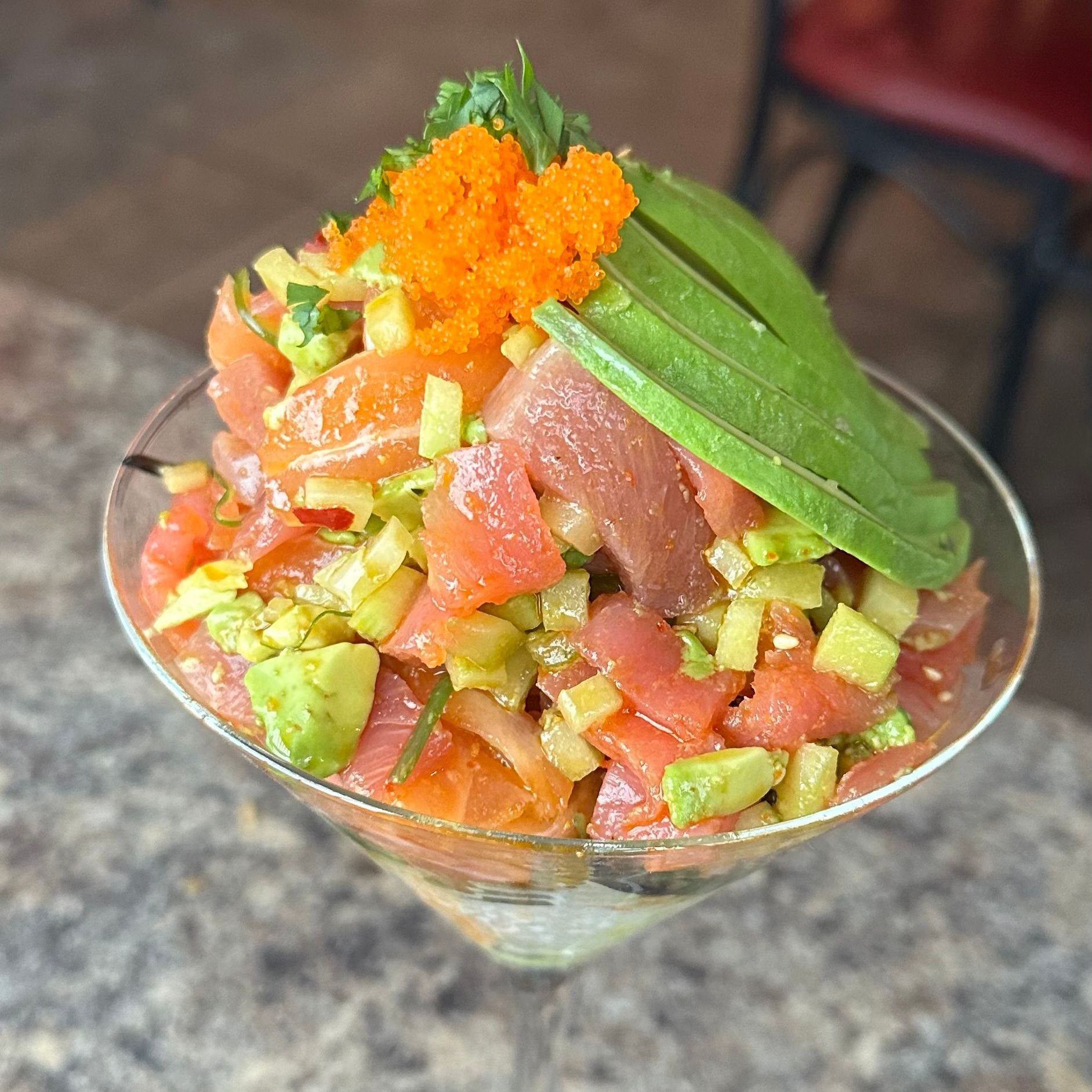 A close up of a salad in a martini glass on a table.