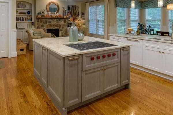 Kitchen with gray island, gas cooktop, white countertops, wood floor, and stone fireplace.