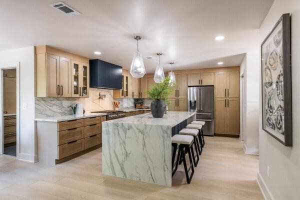 Modern kitchen with marble island, light wood cabinets, and stainless steel appliances.