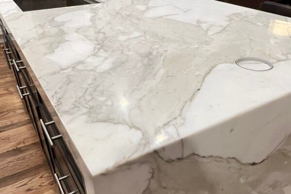 White marble kitchen countertop with gray veining, next to cabinets with stainless steel handles.