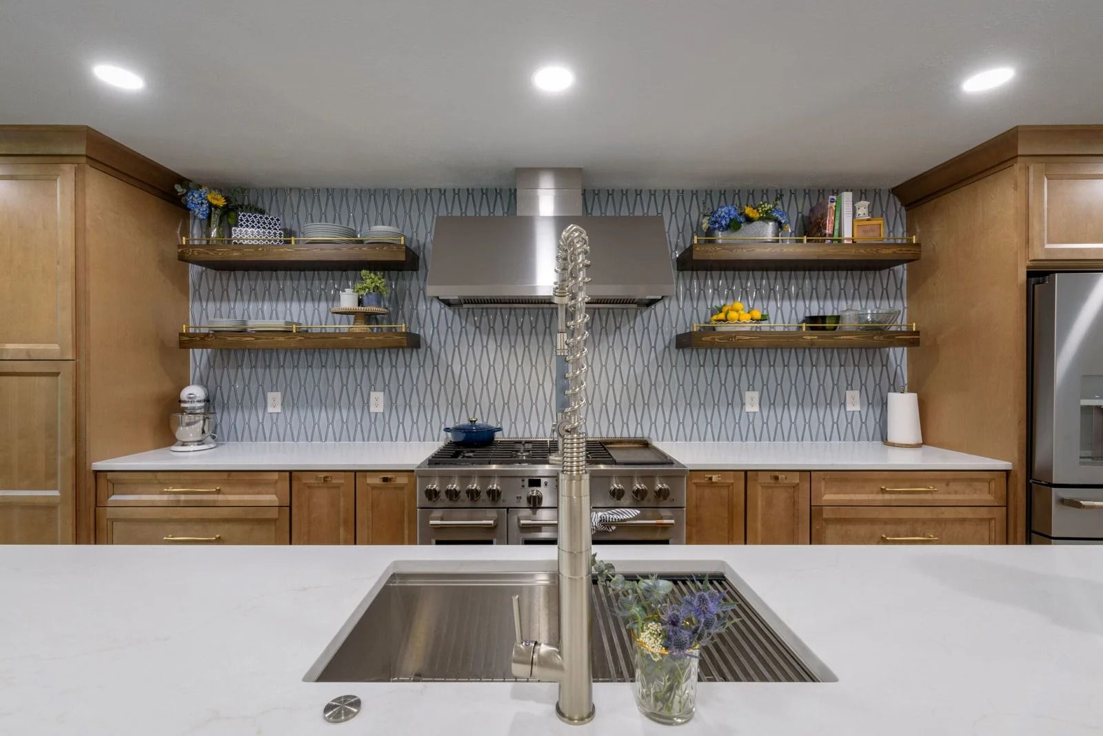 Modern kitchen with stainless steel appliances, wood cabinetry, and blue tiled backsplash.