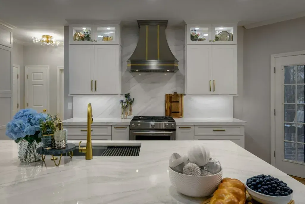 Modern kitchen with white cabinets, stainless steel range hood, and marble countertop.