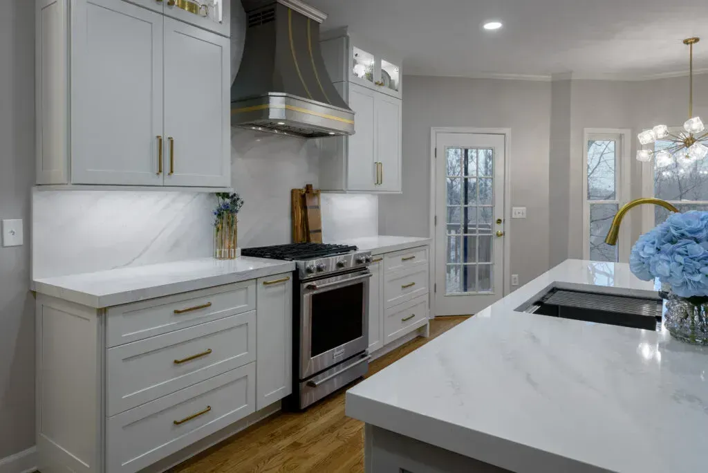 White kitchen with stainless steel appliances, marble countertops, and a windowed door.