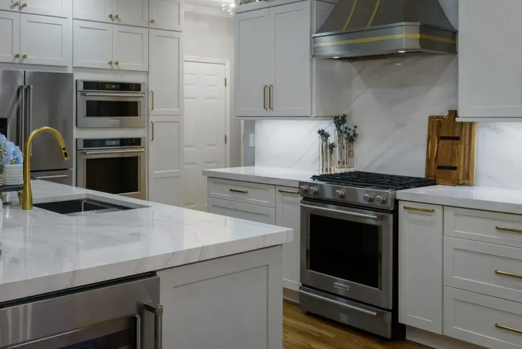 Modern white kitchen with stainless steel appliances, marble countertops, and gold hardware.