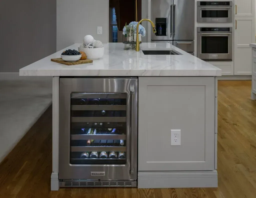 Kitchen island with wine fridge, marble countertop, sink, and cabinets; wooden floor.