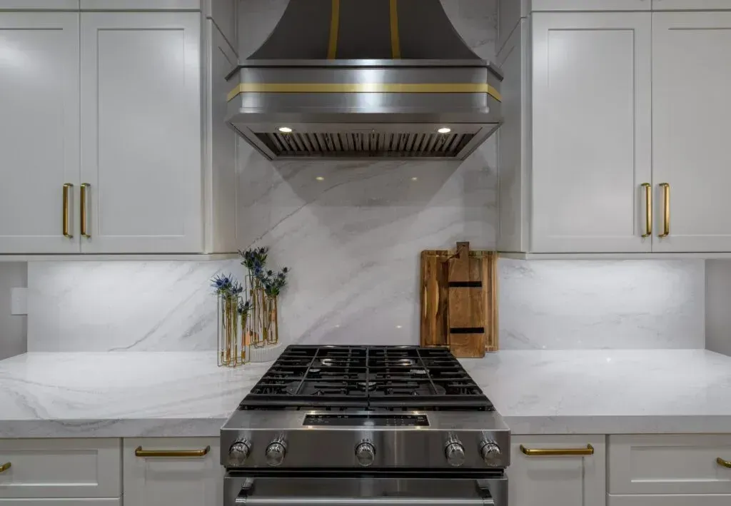 Kitchen with white cabinets, stainless steel stove, range hood, and marble backsplash.