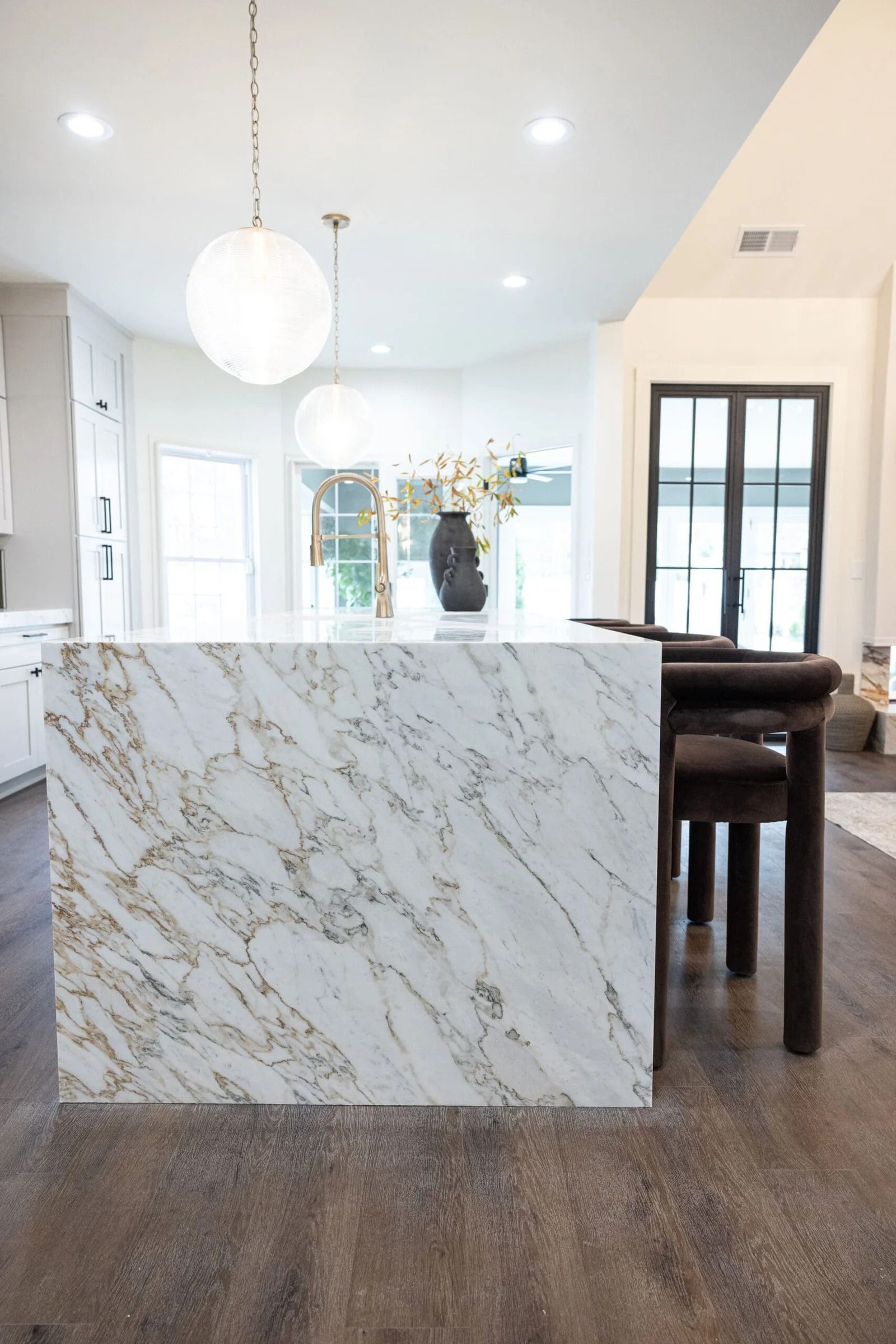 Kitchen island with white marble and brown veining, with modern pendant lights and brown chairs.