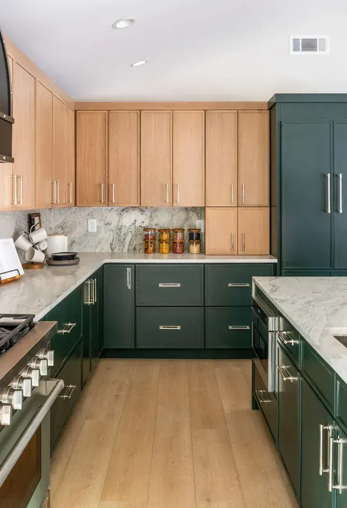 Modern kitchen with light wood upper cabinets, green lower cabinets, and granite countertops.